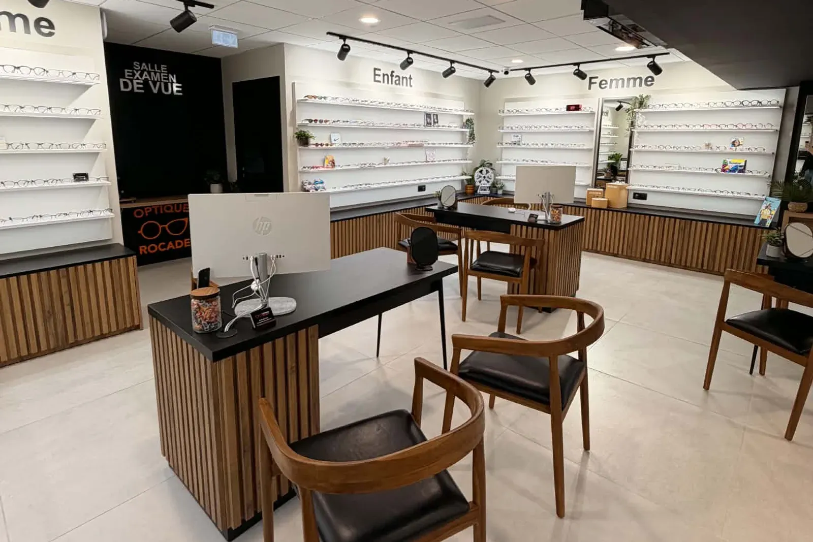 Les rayons enfant et femme du magasin, rangés sur des étagères blanches, et l'entrée noire de la salle d'examen de vue.
