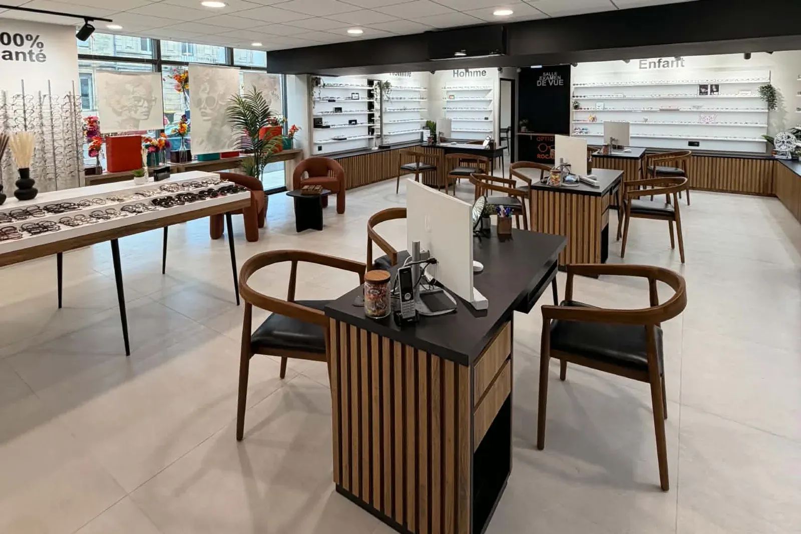 Une longue table de présentation couverte de lunettes de soleil, devant la vitrine du magasin, à côté du présentoir cent pour cent santé.