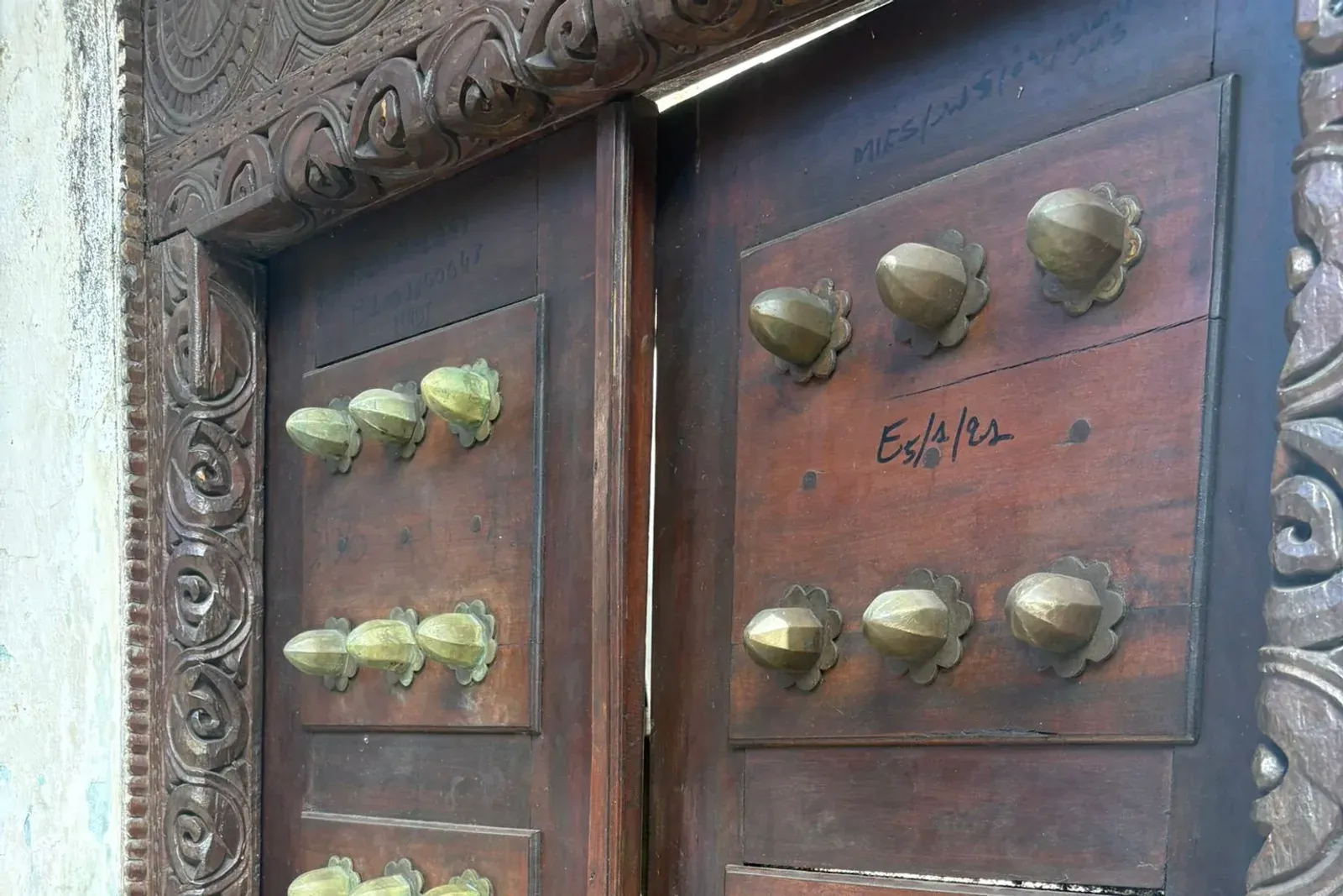 Une porte swahilie en bois sombre, encadrée de motifs sculptés et cloutée de gros ornements de laiton.