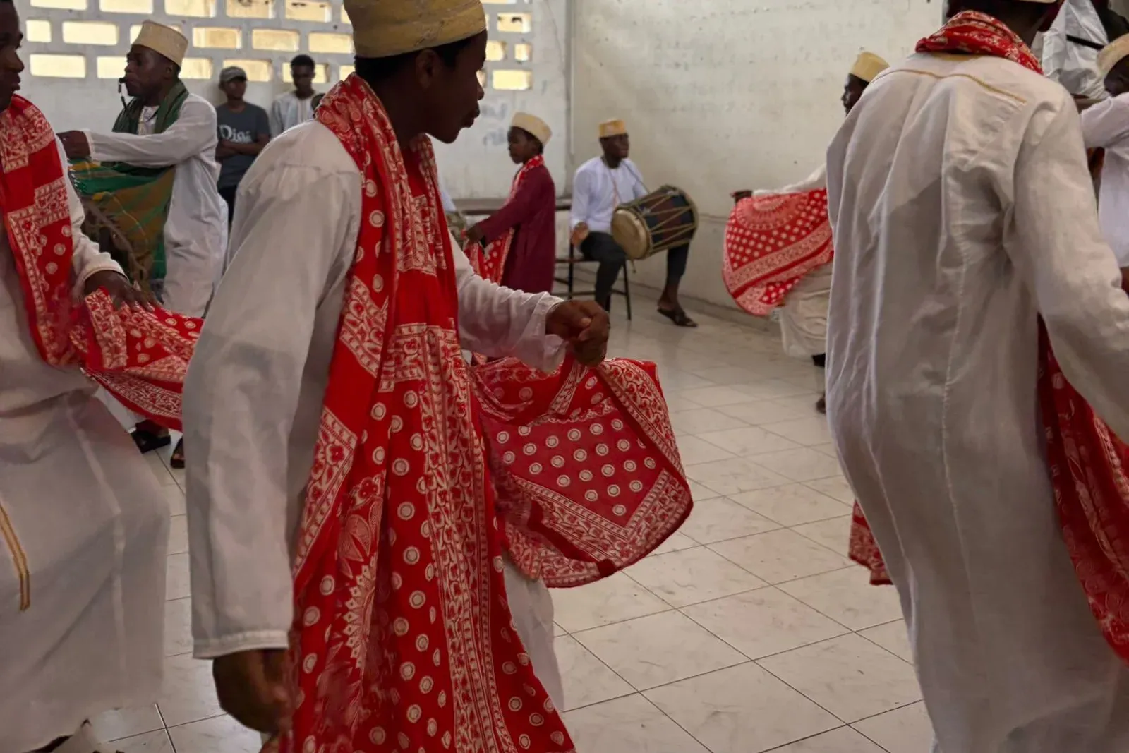 Des danseurs en tunique blanche et châle rouge tournent au son d'un tambour, lors d'une danse traditionnelle comorienne.
