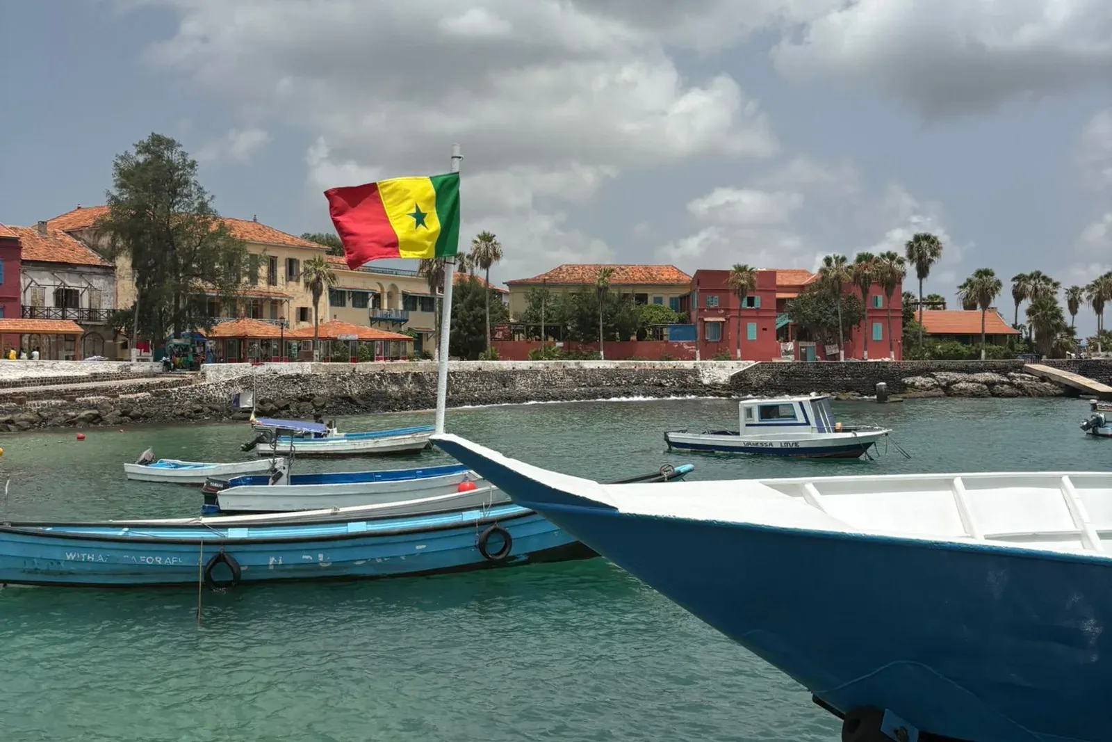 Le drapeau sénégalais flotte à la proue d'une chaloupe, devant les maisons ocre et rouges de l'île de Gorée.
